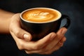 Hands cradling a black coffee cup with latte art