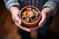 hands cradling bowl filled with beef stew, rustic wooden table