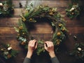 Hands crafting a festive Christmas wreath on wooden table