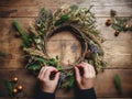 Hands crafting a natural Christmas wreath on a wooden table