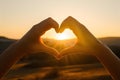 Hands create heart shape in front of scenic sunset with warm and romantic vibe