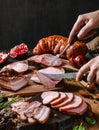 Hands cutting cold meat product, ham, sausage, salami, parma, prosciutto, bacon on wooden cutting board with herb and spices over Royalty Free Stock Photo