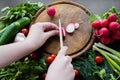 Hands cutting radishes with a white ceramic knife on a round wooden chopping board. Around the board are ripe fresh vegetables: Royalty Free Stock Photo