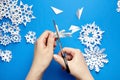 Hands cutting white paper snowflakes over blue Royalty Free Stock Photo
