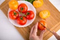 Hands cutting yellow tomato near a white plate with fersh red tomatoes Royalty Free Stock Photo