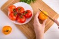 Hands cutting yellow tomato near a white plate with fersh red tomatoes on a wooden board