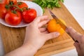 Hands cutting yellow tomato near a white plate with fersh red tomatoes on a wooden board