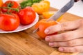 Hands cutting yellow tomato near a white plate with fersh red tomatoes