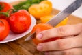 Hands cutting yellow tomato near a white plate with fersh red tomatoes