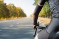 Hands of a cyclist resting on road bike handlebars, road view with copy space.