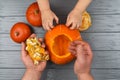 Hands of a daughter and father who pulls seeds and fibrous material from a pumpkin before carving for Halloween. Party