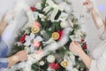 hands decorate festive a Christmas tree garland with lights, glowing bulbs, toys, bows,knitted shoes, balls, poinsettia