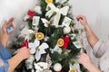 hands decorate festive a Christmas tree garland with lights, glowing bulbs, toys, bows,knitted shoes, balls, poinsettia
