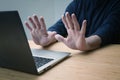 Hands in defensive gesture against a laptop computer, avoiding further work on a hacked system or other danger and offence, online