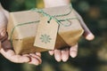 Hands delivering a Christmas gift wrapped in recycled paper with nature`s blur. Ecological and handmade gift concept Royalty Free Stock Photo