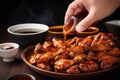 hands dipping chicken wing into honey bbq sauce
