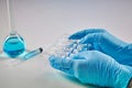 Hands in disposable gloves holding set of five ampoules with liquid. Medical flask with blue chemical reagent, syringe