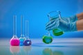 Hands in disposable gloves pouring green liquid from beaker into medical flask. Colorful chemical reagents, blue