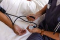 Hands of diverse male doctor taking blood pressure of senior male patient in bed at home Royalty Free Stock Photo