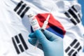 The hands of a doctor holding the Cobid-19 vaccine with blue gloves against the backdrop of the Taegeukgi