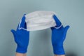 The hands of a doctor, nurse or scientist in blue gloves holds a medical mask for protection against infection isolated on a gray- Royalty Free Stock Photo