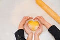 hands with dough in the shape of a heart, flour and eggs on the table.