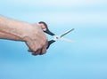 In the hands of an elderly man, scissors cutting something. An old man demonstrates how to cut with scissors on a blue background