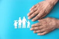 hands of an elderly man and a silhouette of a family with children cut out of paper on a blue background. the concept of a Royalty Free Stock Photo