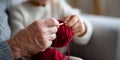 Close-up of elderly and young hands knitting with red yarn indoors, showing skill transfer and bonding through crafting activity Royalty Free Stock Photo