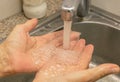 On the hands of an elderly woman, water flows from a shiny faucet. Water is bubbling. Coronovirus protection Royalty Free Stock Photo