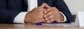 Hands of an elegant man in a suit on a wooden table next to a sheet of paper and a fountain pen. An anonymous hidden official,