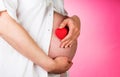 Hands embracing pregnant belly and heart on a pink