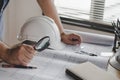 Hands engineer or architect working on blueprint and white safety helmet on workplace desk