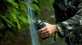 Hands of European young hiker hold glass, draws water from waterfall for drinking, in middle of rainforest