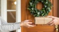 Hands exchanging a beautifully wrapped parcel at a front door, adorned with a festive wreath, symbolizing the joy of delivery and Royalty Free Stock Photo