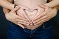 Hands of father and mother on pregnant belly of woman showing heart shape Royalty Free Stock Photo