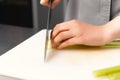 Hands of a female chef are cutting fresh green celery on a plastic board. Royalty Free Stock Photo