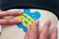 The hands of a female physiotherapist apply adhesive elastic therapeutic tape to the female abdominal muscle of a young adult slim