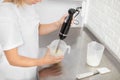 Hands of female professional confectioner holding the hand blender, immersed in the cream, and pressing the power button