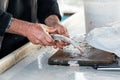 Worn hands of a fisherman cleaning fresh raw fish on a wooden cutting board over the counter Royalty Free Stock Photo