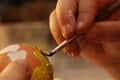 Hands of five years old girl painting yellow heart on blowed easter egg with thin brush