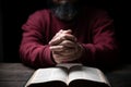 Hands folded in prayer on a Holy Bible in church concept for faith, spirituality and religion, man praying in morning. Man hand