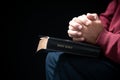 Hands folded in prayer on a Holy Bible in church concept for faith, spirituality and religion, man praying in morning. Man hand