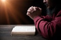 Hands folded in prayer on a Holy Bible in church concept for faith, spirituality and religion, man praying in morning. Man hand