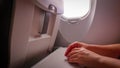 Hands on the folding table of the chair in the cabin of the aircraft near the porthole