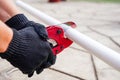 The hands of the foreman hold metal scissors for cutting plastic water pipes outside.