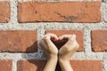 Hands forming a heart with hands forming a heart shadow on a brick wall in the sunshine.