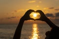 Hands forming a heart shape with sunset silhouette near sea water, close up Royalty Free Stock Photo