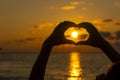 Hands forming a heart shape with sunset silhouette near sea water, close up Royalty Free Stock Photo