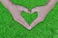 Hands forming a shape heart on green lawn